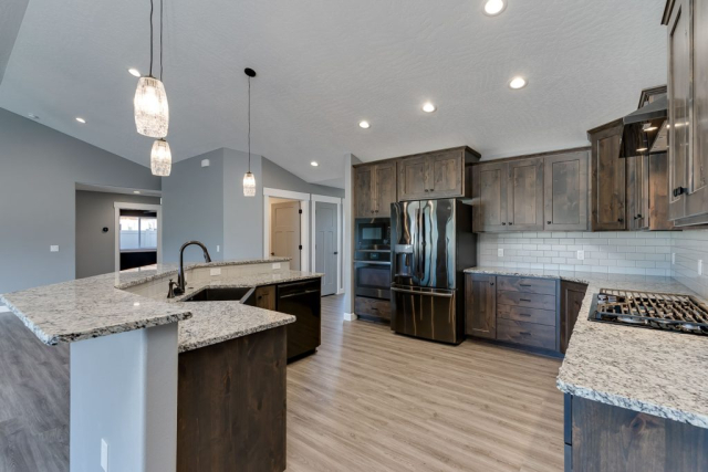 A spacious and modern kitchen designed with an open layout, gray cabinets, stainless steel appliances, pendant lighting, and a large center island with a sink.