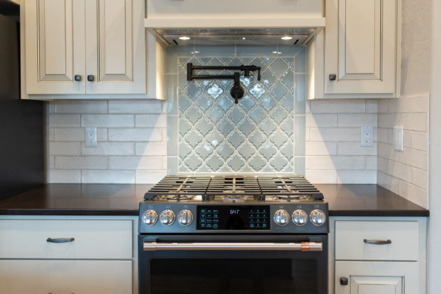A modern kitchen designed featuring stainless steel appliances with a focus on a sleek gas stove-top and an elegant, decorative backsplash.