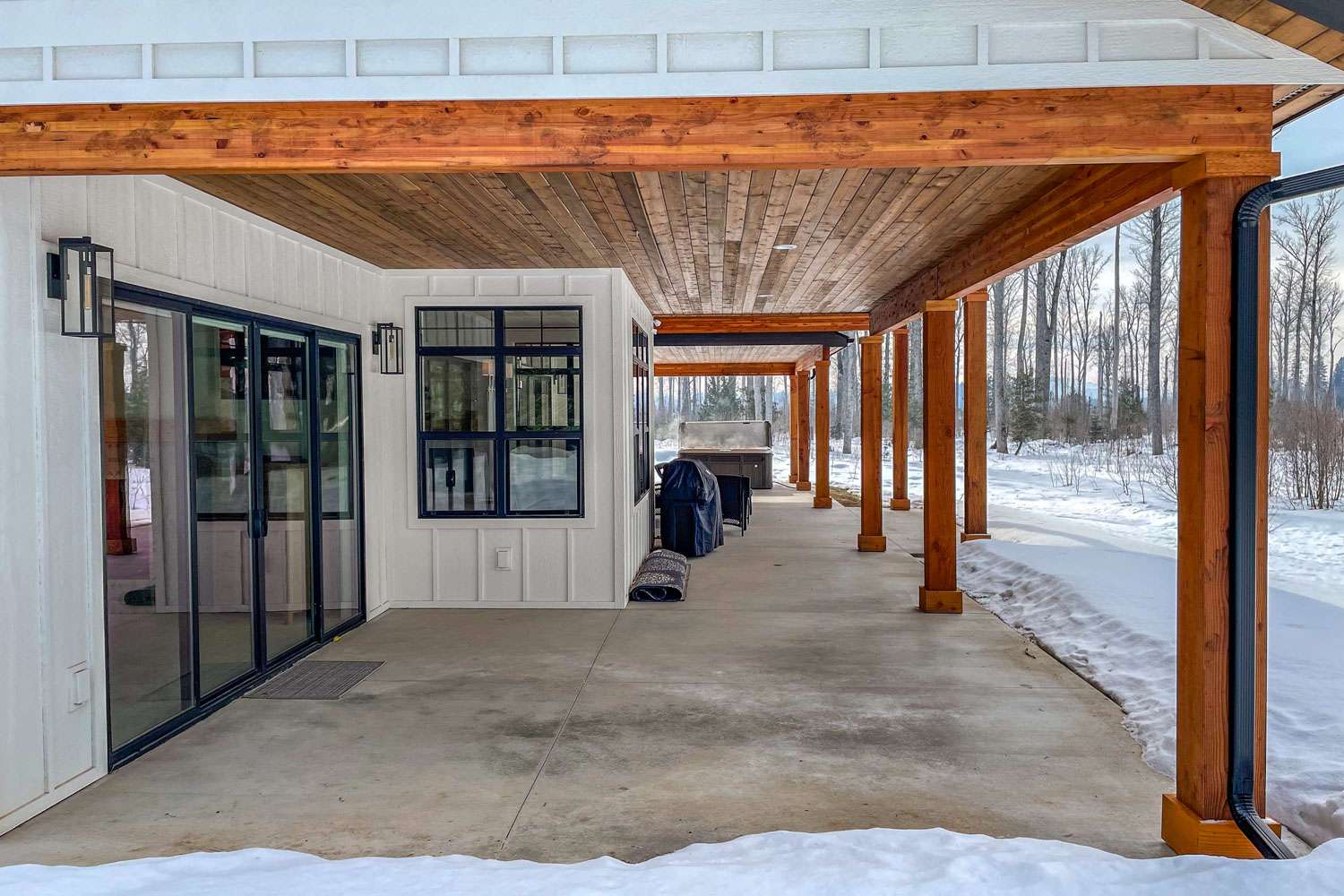 A modern home's designed covered patio with wooden beams and a snow-covered landscape in the background.