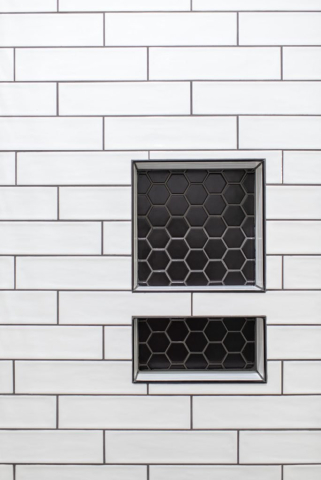 2111 E Garwood Rd A tiled wall with clean white rectangular tiles and dark grout features two built-in niches. The niches, lined with designer black hexagonal tiles, create a striking contrast with the surrounding white tiles. One niche is square, while the other is a smaller rectangle below it, adding quality detail.