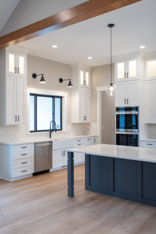 2111 E Garwood Rd A modern kitchen in a custom home featuring white cabinets with black handles, stainless steel appliances, a black faucet, and light-gray subway tile backsplash. The island has a dark base with a light countertop, and two pendant lights hang overhead. Light wooden flooring adds to the spacious feel throughout.