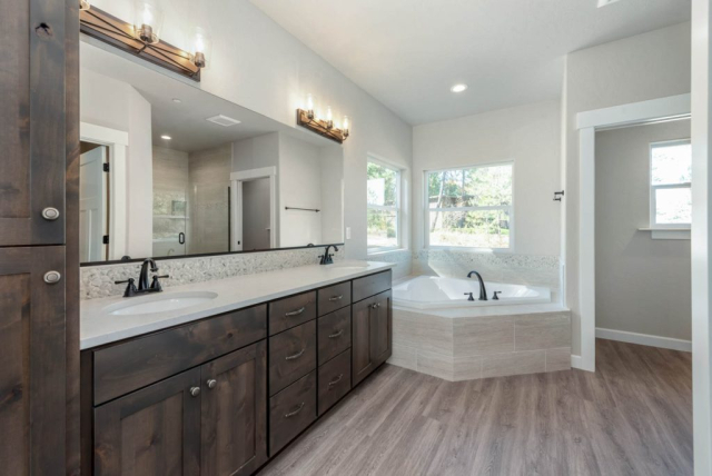 3851 W Grandview Ave A stylish modern bathroom in a custom home featuring dual sinks, a large mirror, sleek cabinetry, a luxurious bathtub, and sophisticated lighting fixtures.