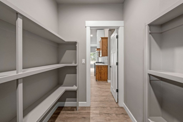 Peacock Lane by Premier Quality Homes A modern hallway with empty white custom-built shelves leading to a kitchen with wooden cabinets.