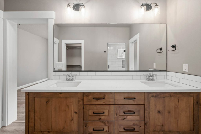 Peacock Lane by Premier Quality Homes Modern bathroom interior with dual sinks, wooden cabinetry, and a view into a custom-designed walk-in shower.