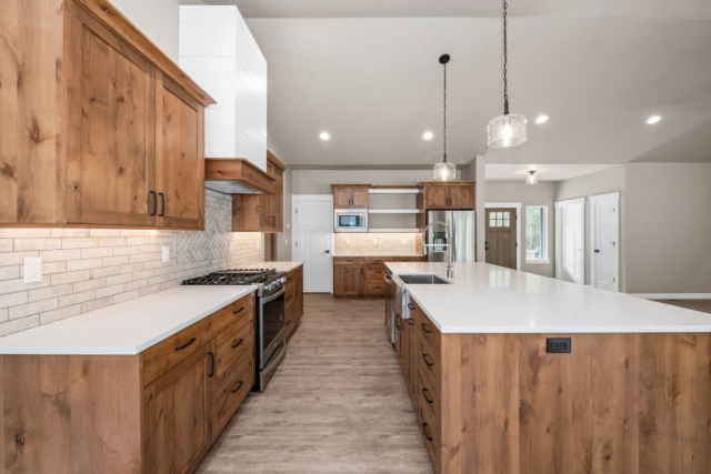 Spacious modern kitchen with custom-built natural wood cabinetry, white countertops, stainless steel appliances, and elegant pendant lighting.