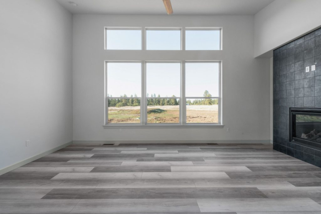 16930 W Rolling Hills Lane Spacious modern living room with large windows providing plenty of natural light, a sleek fireplace, and stylish gray plank flooring, designed awaiting furniture and personal touches to become a cozy home.
