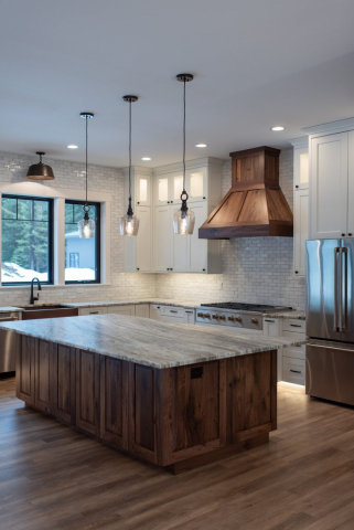 25362 N Werre Rd A modern kitchen in a custom home with a large wooden island featuring a marble countertop. Three designer pendant lights hang above the island. The space has white cabinetry, a stainless steel refrigerator, a wooden range hood, and a window letting in natural light.