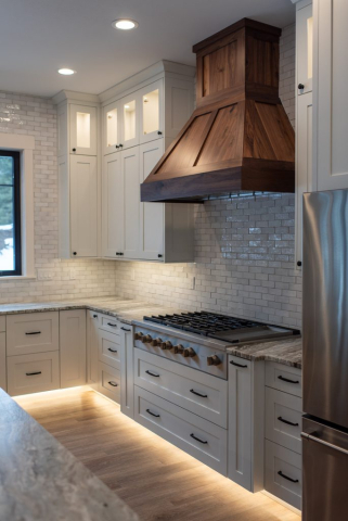 25362 N Werre Rd A modern kitchen in a custom home featuring white cabinets, quality stainless steel appliances, and a large wooden range hood. The backsplash is made of white subway tiles, and under-cabinet lighting illuminates the countertops and wooden floor. A window provides natural light.