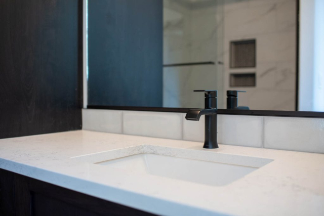 25299 N Werre Rd A sleek, modern bathroom sink with a matte black faucet set against a marble countertop and dark cabinetry, reflecting a minimalistic and custom design aesthetic.