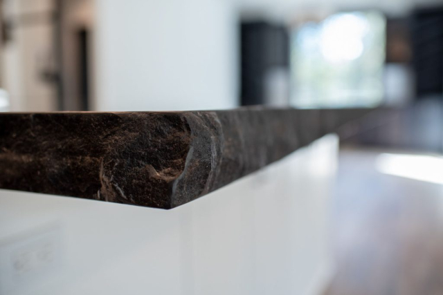 25299 N Werre Rd Close-up of a polished brown marble countertop with a blurred modern kitchen interior in the background, designed for custom homes.