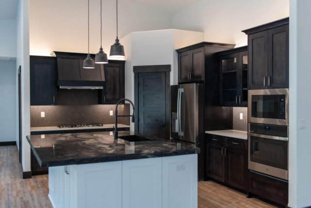 Modern kitchen designed with dark wood cabinets, stainless steel appliances, and a contrasting white island with a sleek black countertop.