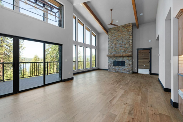 Woodlake Drive by Premiere Quality Homes Spacious living room with tall ceilings, large windows offering a new view of nature, hardwood floors, and a stone fireplace.