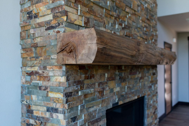 Woodlake Drive by Premiere Quality Homes A close-up view of a new fireplace with a rustic wooden mantel over a multicolored stone surround in custom-built homes.