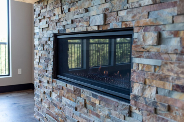 Woodlake Drive by Premiere Quality Homes A custom-built modern gas fireplace set into a wall with multicolored stone tiles, providing a cozy ambiance to a contemporary living space.