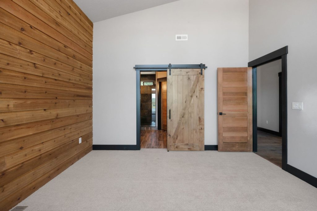 Woodlake Drive by Premiere Quality Homes A spacious room with light carpeting featuring a wooden accent wall and two barn-style sliding doors, designed with a keen eye for detail, one of which is open, leading to adjacent rooms.