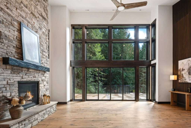 parade-house-10 Living room with an entire wall of windows on one side, next to a stone hearth fireplace.