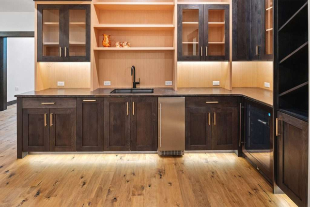 parade-house-35 Modern kitchen with wooden floor, dark wood cabinets, and dark lower cabinets. Built-in shelves and warm lighting creates an inviting atmosphere.
