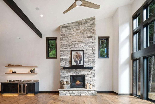 parade-house-9 Living room with an entire wall of windows on one side, next to a stone hearth fireplace.